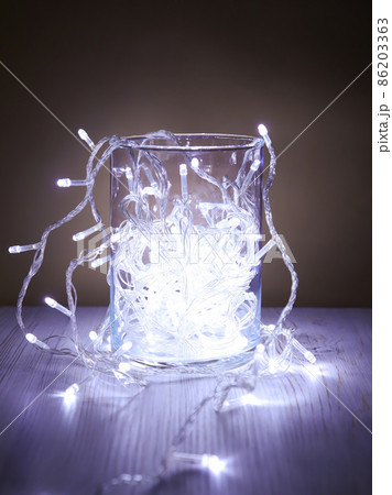 Christmas white garland lights from LED bulbs in glass jar on wooden table background. Front view Christmas white garland lights from LED bulbs in glass jar on wooden table background. Front view 86203363
