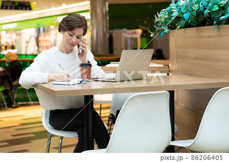 Young attractive brunette woman sitting at a shopping center at a table and working at a computer Young attractive brunette woman sitting at a shopping center at a table and working at a computer 86206405