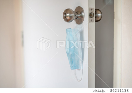 Used protective face mask hanging over a door knob. Used protective face mask hanging over a door knob. 86211158