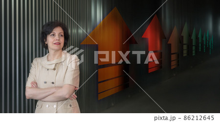 Pretty middle aged business woman in business suit, successful confidence close up head and shoulders portrait against dark wall with up arrows in perspective. 86212645