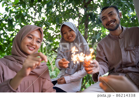 smiling father, mother and daughter lighting fireworks together smiling father, mother and daughter lighting fireworks together 86214338