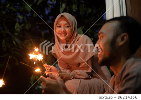 A woman in a headscarf lights fireworks with a man 86214356