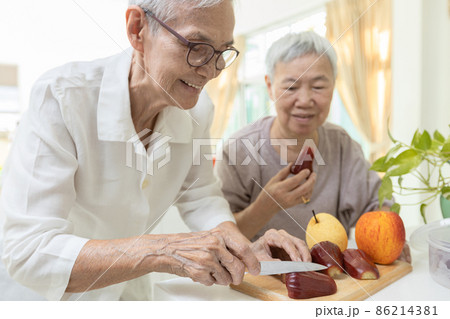 Happy asian senior grandmother cutting the fresh fruit into slices with a knife,healthy elderly people enjoy tasting delicious fruits,preparing healthy meal,cooking,healthy  food,health care concept 86214381