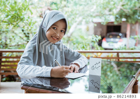 veiled girl smiling writing a happy eid mubarak greeting card 86214893