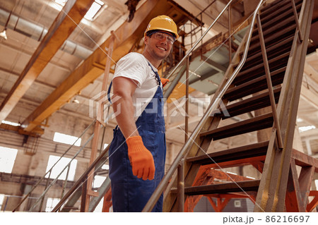 Cheerful male builder standing on stairs in workshop 86216697
