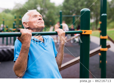 mature cheerful pensioner man doing physical exercises on sports equipped playground mature cheerful pensioner man doing physical exercises on sports equipped playground 86216713