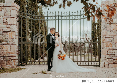 Happy stylish smiling couple walking in Tuscany, Italy on their wedding day. The bride and groom walk down the street by the hands. A stylish young couple walks. Husband and wife communicate nicely 86216884