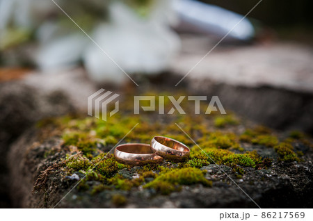Floral arrangement with white flowers, wedding bouquet with a ribbon and two gold rings, lying on a stone. Wedding decor, artwork, florist Floral arrangement with white flowers, wedding bouquet with a ribbon and two gold rings, lying on a stone. Wedding decor, artwork, florist 86217569