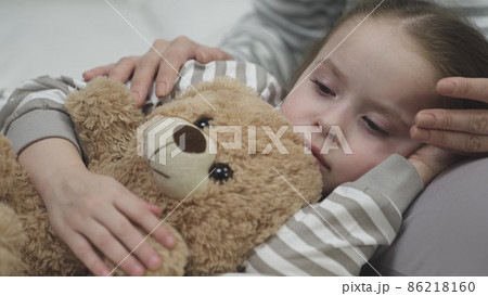 Tired girl falls asleep on mother laps hugging teddy bear Tired girl falls asleep on mother laps hugging teddy bear 86218160