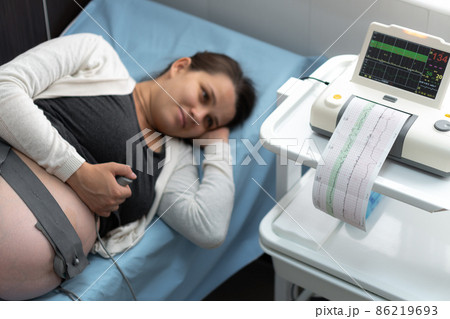 Pregnant Woman On Hospital Couch During Medical Control Cardiotocography. Gynecologist Doctor Hands Turn On Adjust CTG Device Clinic Consultant. Examine Expectant Belly Baby Mother Healthcare Check Up 86219693