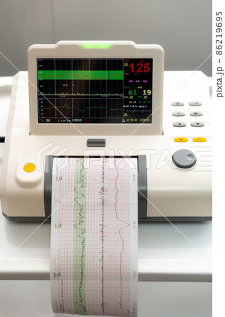 Electronic Cardiotocography Machine Monitoring Fetal Heart Contractions Of Uterus. Printing Cardiogram Report Coming Out Electrocardiogram In Labor Ward During Pregnancy. Medical Diagnostic Equipment 86219695
