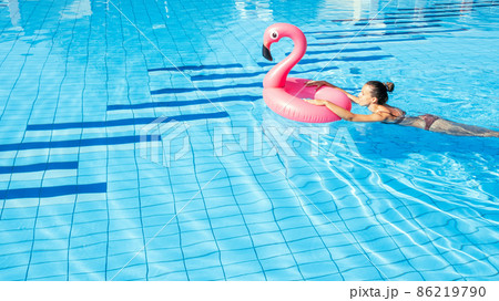 Summer fun. Happy young sexy girl in bikini swimsuit with pink flamingo float in blue pool water. Having fun and enjoying travel vacation. Swimming pool water. Summer fun. Happy young sexy girl in bikini swimsuit with pink flamingo float in blue pool water. Having fun and enjoying travel vacation. Swimming pool water. 86219790