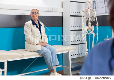 Portrait of sick sick pensioner woman patient standing on bed in hospital office looking into camera Portrait of sick sick pensioner woman patient standing on bed in hospital office looking into camera 86220965
