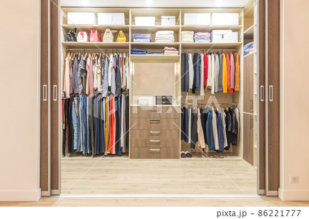 Modern wooden wardrobe with clothes hanging on rail in walk in closet 86221777
