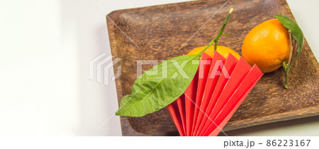 Chinese New Year, composition with tangerines, funny origami made of red paper on a dark wooden plate on a white background, space for text on the left Chinese New Year, composition with tangerines, funny origami made of red paper on a dark wooden plate on a white background, space for text on the left 86223167