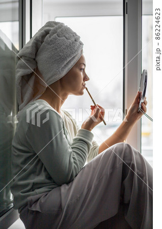 Morning woman in towel on hairs doing makeup skin tone foundation use brush looking at mirror Morning woman in towel on hairs doing makeup skin tone foundation use brush looking at mirror 86224623