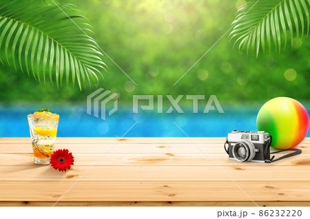 Wooden table top with with accessories glass of fruit juice camera and beach ball isolate with blured swimming pool background with palm leaves as frame montage for product advertisement 86232220
