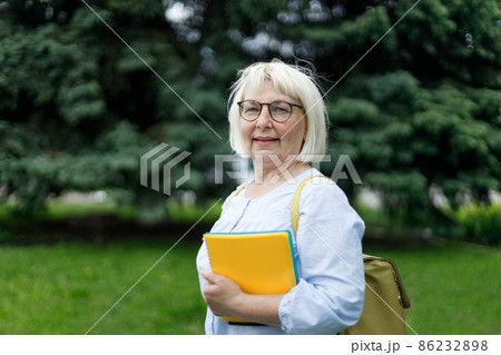 Smiling blonde teacher woman lady 40s 50s years old wearing eyeglasses standing hold notepads looking camera outdoors 86232898