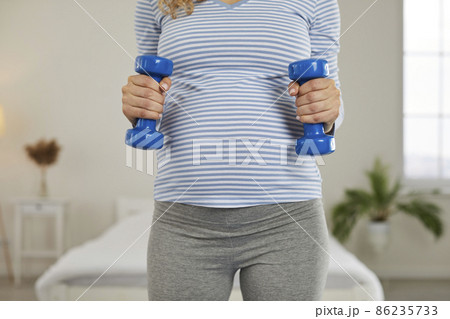 Close up crop of healthy young pregnant woman hold dumbbells do sports. Female train exercise workout during pregnancy time. Physical activity and motherhood concept. Close up crop of healthy young pregnant woman hold dumbbells do sports. Female train exercise workout during pregnancy time. Physical activity and motherhood concept. 86235733