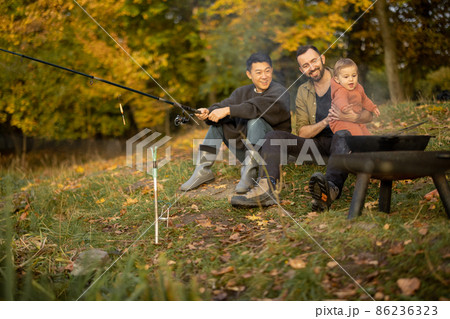 Male friends resting and fishing on lake coast 86236323