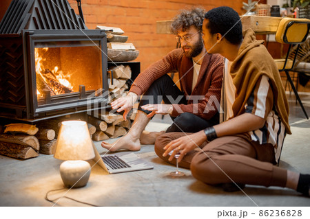 Two men sitting together by the burning fireplace at cozy home Two men sitting together by the burning fireplace at cozy home 86236828
