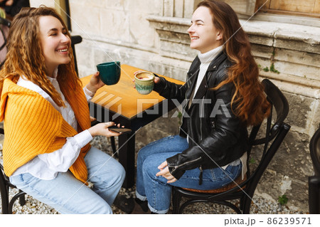 Cheerful female best friend share multimedia files on smartphones spending free time together,smiling hipster girls drinking coffee, sitting at terrace cafe. Cheerful female best friend share multimedia files on smartphones spending free time together,smiling hipster girls drinking coffee, sitting at terrace cafe. 86239571