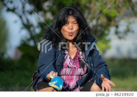 An Asian middle aged woman playing calling a puppy. Soft, blurry background An Asian middle aged woman playing calling a puppy. Soft, blurry background 86239920