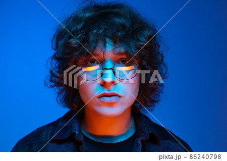 Close-up face of sad man, student looking at camera isolated on blue background in neon light. Concept of emotions, study, education, fashion Close-up face of sad man, student looking at camera isolated on blue background in neon light. Concept of emotions, study, education, fashion 86240798