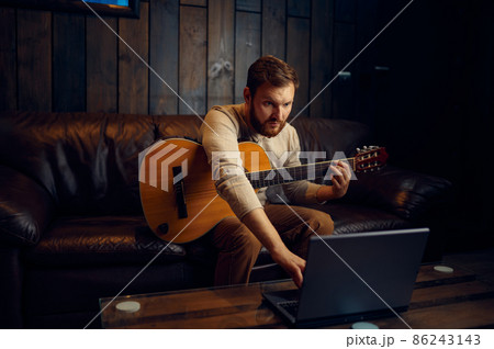 Young man learning playing guitar through internet Young man learning playing guitar through internet 86243143