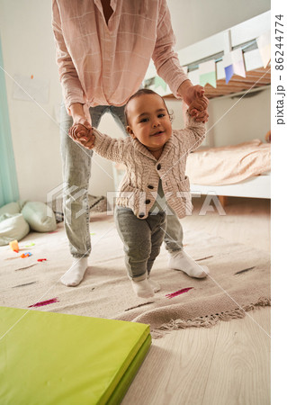 Mother watching at her newborn baby son taking first steps at home at the bedroom Mother watching at her newborn baby son taking first steps at home at the bedroom 86244774