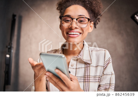 Joyful young woman looking at camera, holding smartphone and chatting 86245639