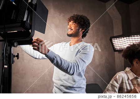 Cheerful multiracial guy standing in front of the lighting equipment and correcting 86245656