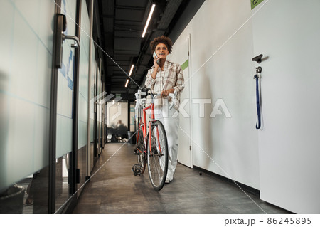 Multiracial curly woman having call at her smartphone while standing with her bicycle Multiracial curly woman having call at her smartphone while standing with her bicycle 86245895
