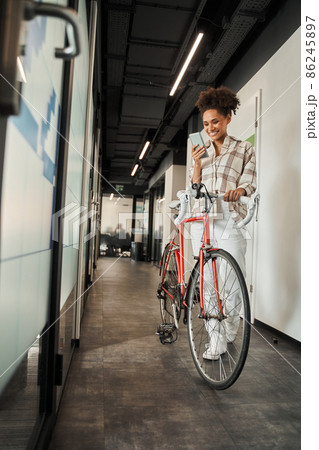 Multiracial woman looking at her cell phone screen while standing with her bicycle 86245897