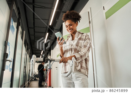 Female looking at the smartphone screen while standing with her bicycle at the hall Female looking at the smartphone screen while standing with her bicycle at the hall 86245899