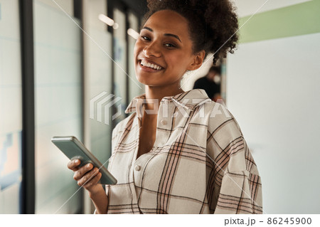 Cute female holding smartphone and smiling cheery to the camera Cute female holding smartphone and smiling cheery to the camera 86245900