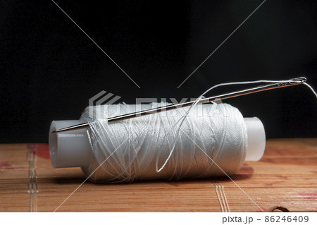 The thread is threaded through the eye of a sewing needle.Sewing and needlework classes.Workshop of hand craft and handmade.Workplace of the textile industry.The embroidery needle is stuck in a bobbin 86246409