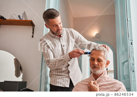 Middle aged son cutting hair to his retirement father by himself at home while chatting Middle aged son cutting hair to his retirement father by himself at home while chatting 86246534