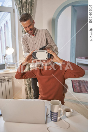 Handsome adult caucasian man adjusting his VR headset with toothy smile at his senior Handsome adult caucasian man adjusting his VR headset with toothy smile at his senior 86246614