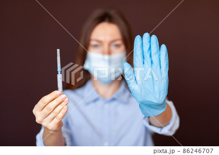Coronavirus concept. Girl wearing mask for protection from disease and show stop hands gesture for stop corona virus outbreak. Stop the pandemic with vaccination. There is a syringe in the girl's hand Coronavirus concept. Girl wearing mask for protection from disease and show stop hands gesture for stop corona virus outbreak. Stop the pandemic with vaccination. There is a syringe in the girl's hand 86246707