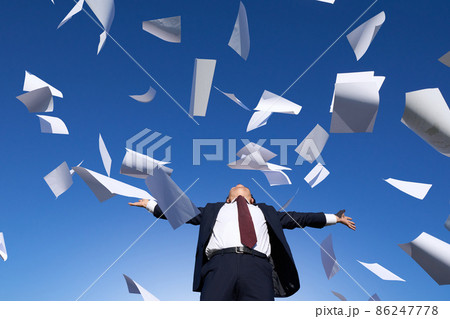 書類が舞う青空のもとで両手を広げるスーツ姿の男性 86247778