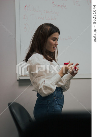 Young female english language teacher with a red marker in a white blouse standing in front of a white board 86251044