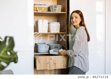 Smiling female putting clothes wardrobe comfortable vertical storage system Marie Kondo method Smiling female putting clothes wardrobe comfortable vertical storage system Marie Kondo method 86253318