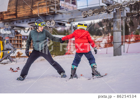 Boy learning to ski, training and listening to his ski instructor on the slope in winter Boy learning to ski, training and listening to his ski instructor on the slope in winter 86254534