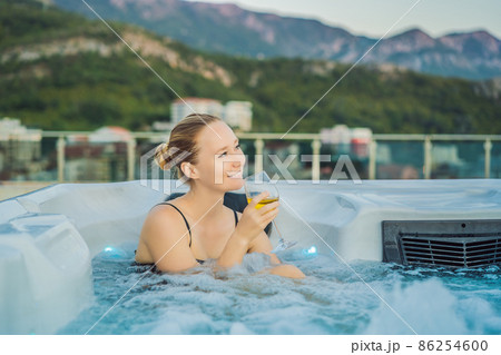 Portrait of young carefree happy smiling woman relaxing at hot tub during enjoying happy traveling moment vacation life against the background of green big mountains Portrait of young carefree happy smiling woman relaxing at hot tub during enjoying happy traveling moment vacation life against the background of green big mountains 86254600