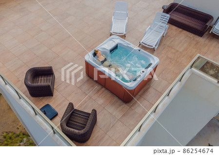 Drone view. Portrait of young carefree happy smiling woman relaxing at hot tub during enjoying happy traveling moment vacation life against the background of green big mountains Drone view. Portrait of young carefree happy smiling woman relaxing at hot tub during enjoying happy traveling moment vacation life against the background of green big mountains 86254674