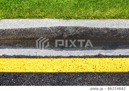 puddle on drain canal near asphalt road with stormwater on the road side with ditch for water after rain and glade of green lawn along highway with yellow marking. 86254682