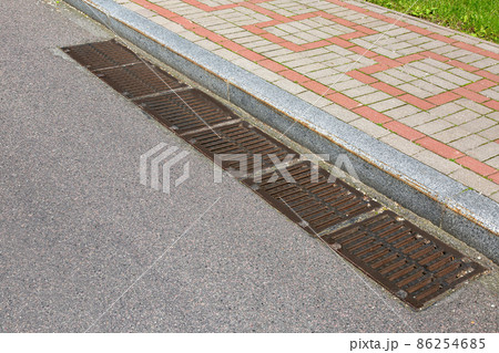 rectangular manholes of the lattice of the drainage system for drainage of rainwater from the road surface with an asphalt road at granite curb with stone tile sidewalk on sidewalk. 86254685