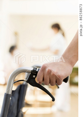 車いすを押す男性介護士の手元と奥で熱を測るシニア 車いすを押す男性介護士の手元と奥で熱を測るシニア 86258873