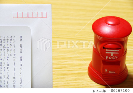 木目のテーブルに置いた郵便ポスト形の貯金箱と礼文の封筒 86267100